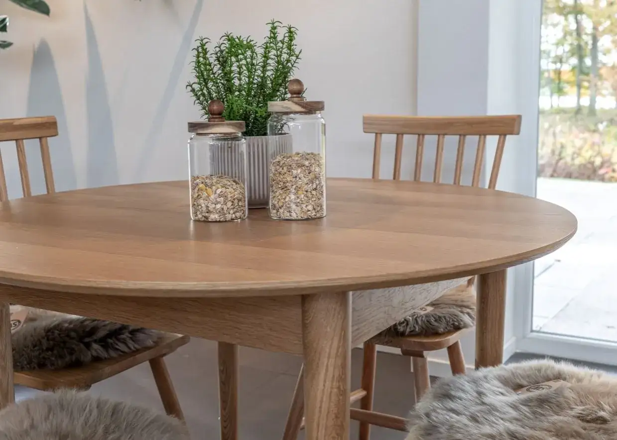 Runt matbord i tr&auml; med tv&aring; glasburkar fyllda med m&uuml;sli och en gr&ouml;n v&auml;xt. Mysiga f&aring;rskinn p&aring; stolarna ger inspiration.