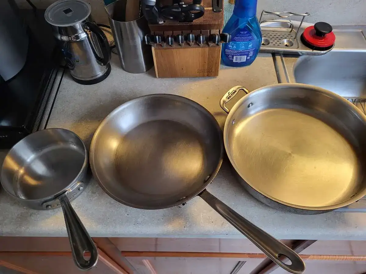 Tre stekpannor p&aring; en b&auml;nk: en liten i rostfritt st&aring;l, en st&ouml;rre kolst&aring;l och en stor rostfri. Valet mellan kolst&aring;l vs rostfritt st&aring;l stekpanna beror p&aring; matlagningen.