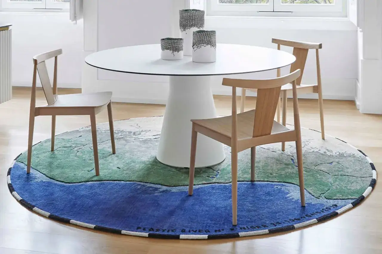Rund matta under matbord med stolar. Mattan har ett m&ouml;nster som liknar ett landskap med bl&aring;tt och gr&ouml;nt.