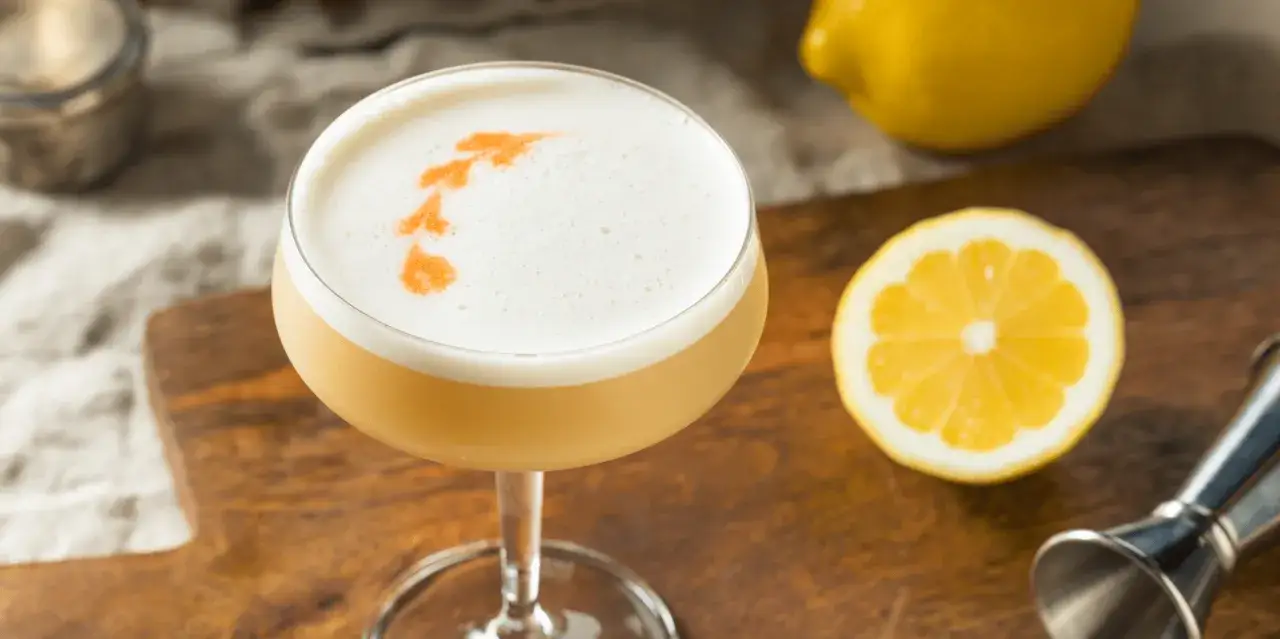 En läcker drink med skummig topp, dekorerad med orange mönster. Bredvid ligger en citronskiva och en hel citron, redo för mer sifon till drinkar.