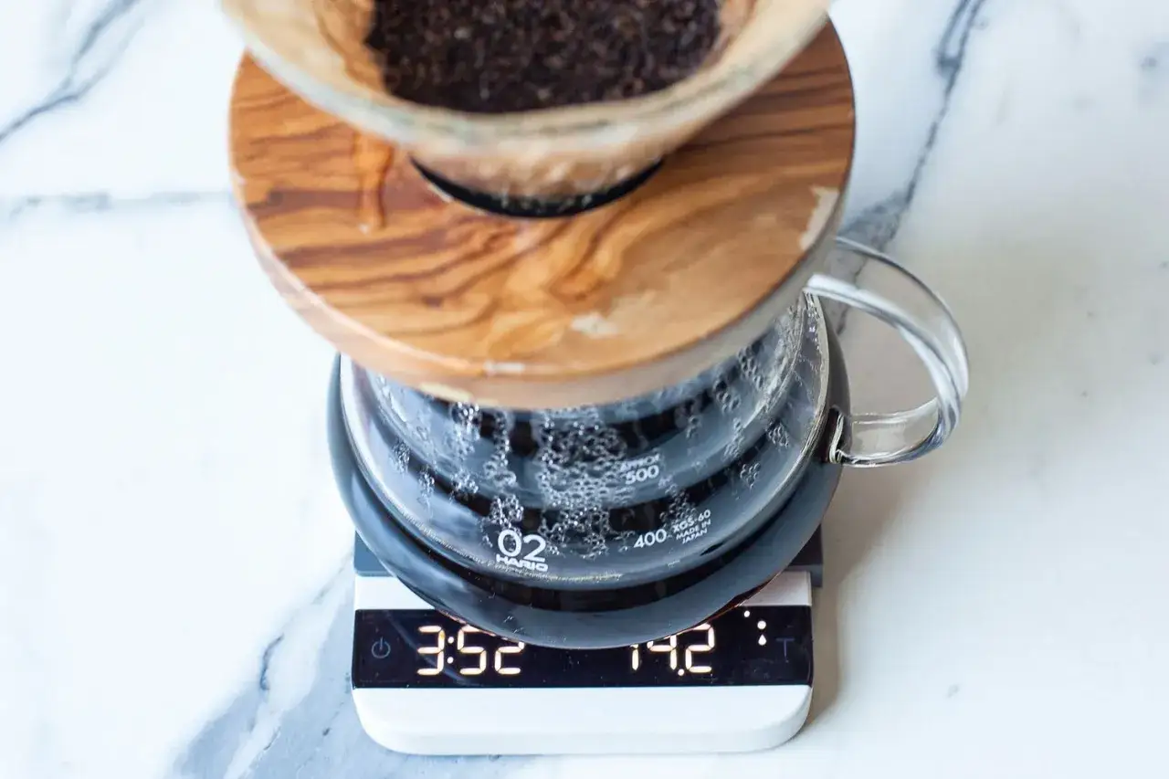 Kaffebryggning med V60. Kaffebryggaren st&aring;r p&aring; en v&aring;g som visar tid och vikt, vilket indikerar noggrann kaffe dosering.