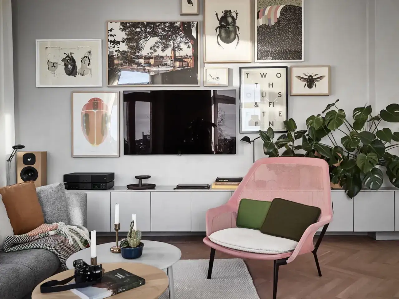 En modern inredning där man valt att placera tv:n centralt på väggen, omgiven av konst. En rosa fåtölj och gröna växter ger färg.