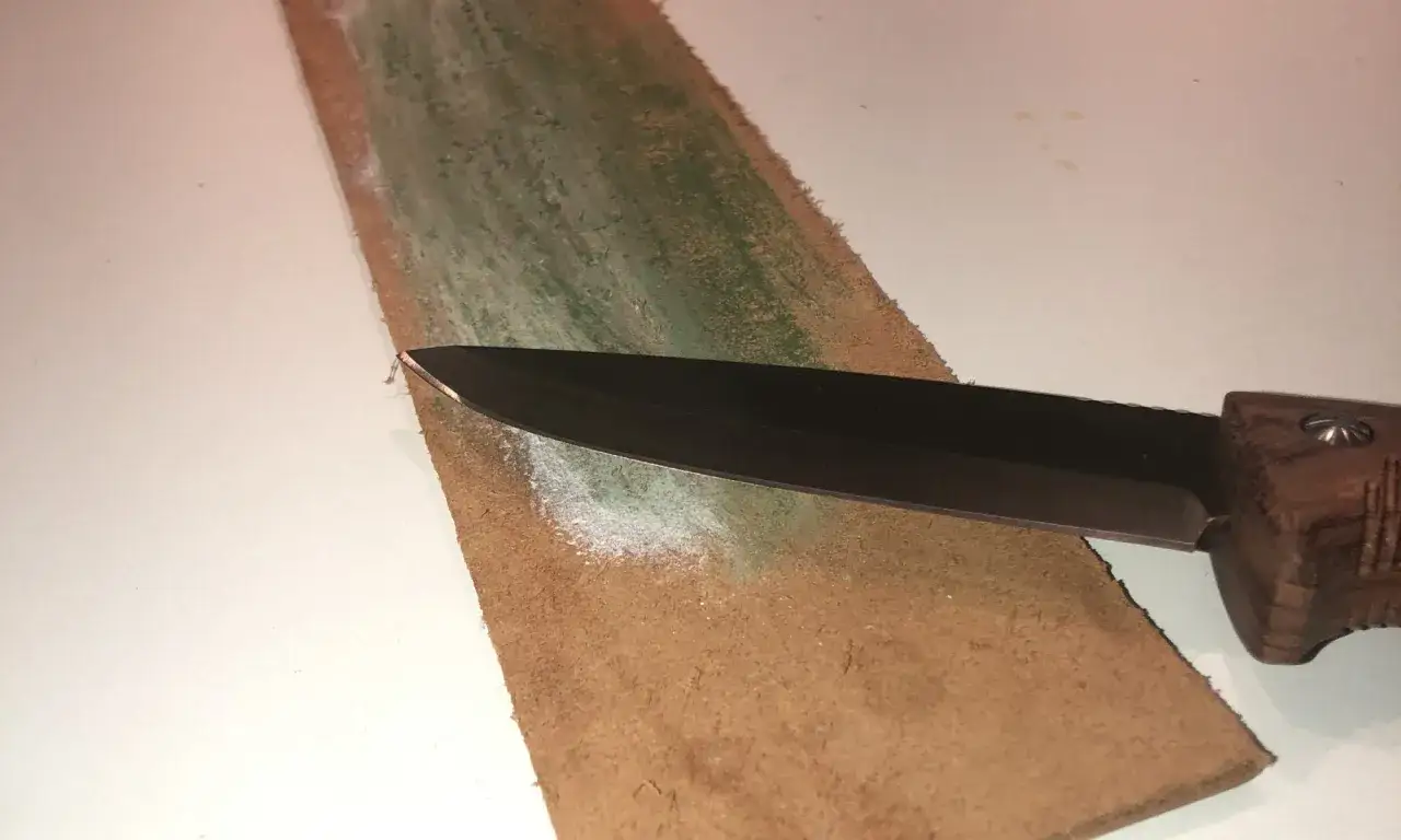 En kniv med trähandtag striglas mot ett läderbälte med polerpasta.