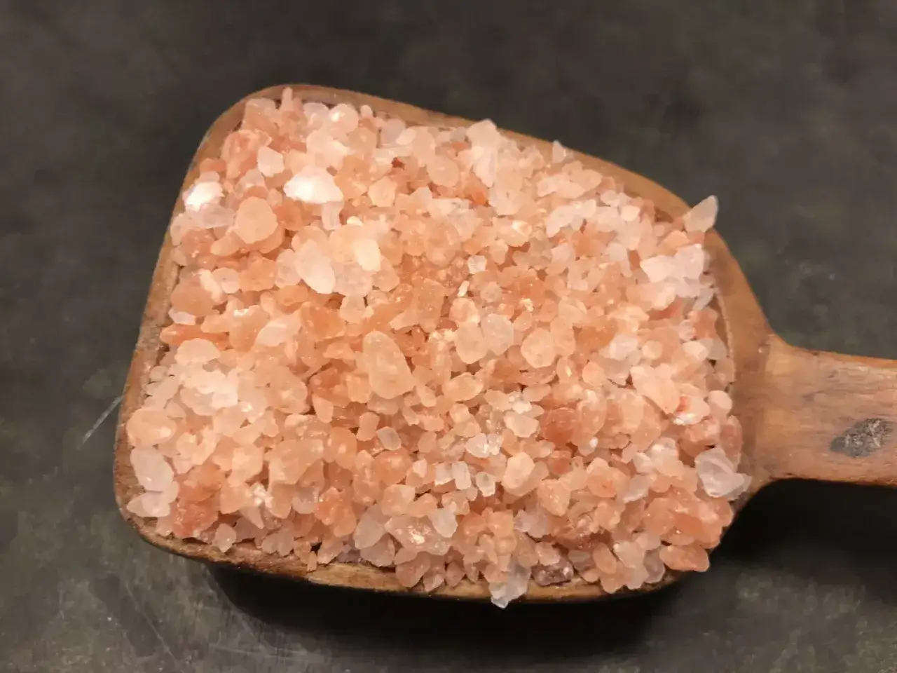 En träskopa fylld med rosa Himalayasalt, redo att malas i en saltkvarn för att ge smak åt maten.