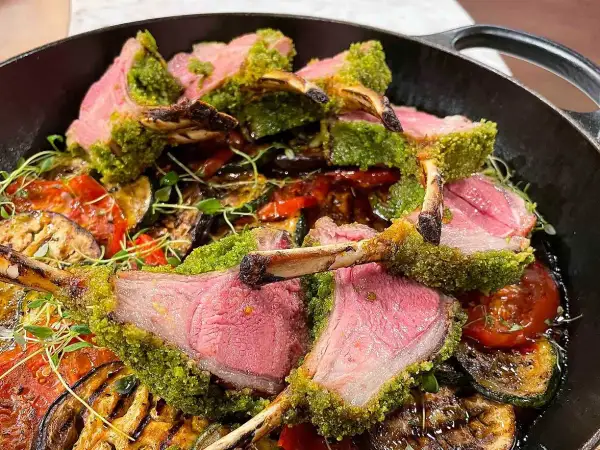 Saftigt lamm med perfekt lamm temperatur, täckt av gröna örter, serveras med grillade grönsaker i en gjutjärnspanna.