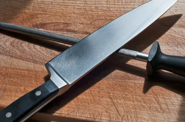 En kockslipar kniv mot ett skärpstål på en träskärbräda.