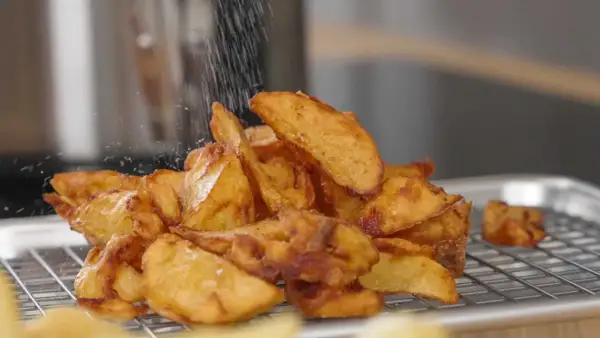 Krispiga pommes frites, perfekt frityr temp, strös salt över en hög gyllene potatisklyftor på ett galler.