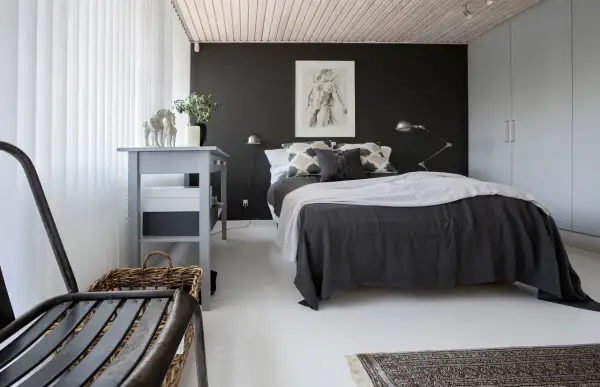 Ett modernt svart sovrum med en stor säng, konst på väggen och en grå byrå.