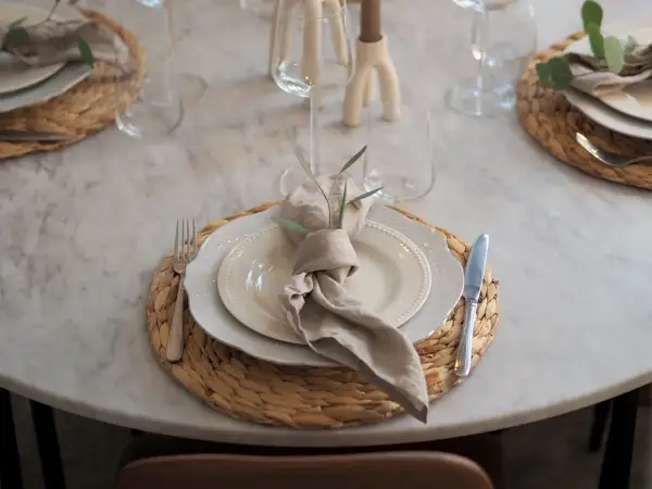 En modern juldukning med linneservetter, vita tallrikar och glas på en marmorbord.